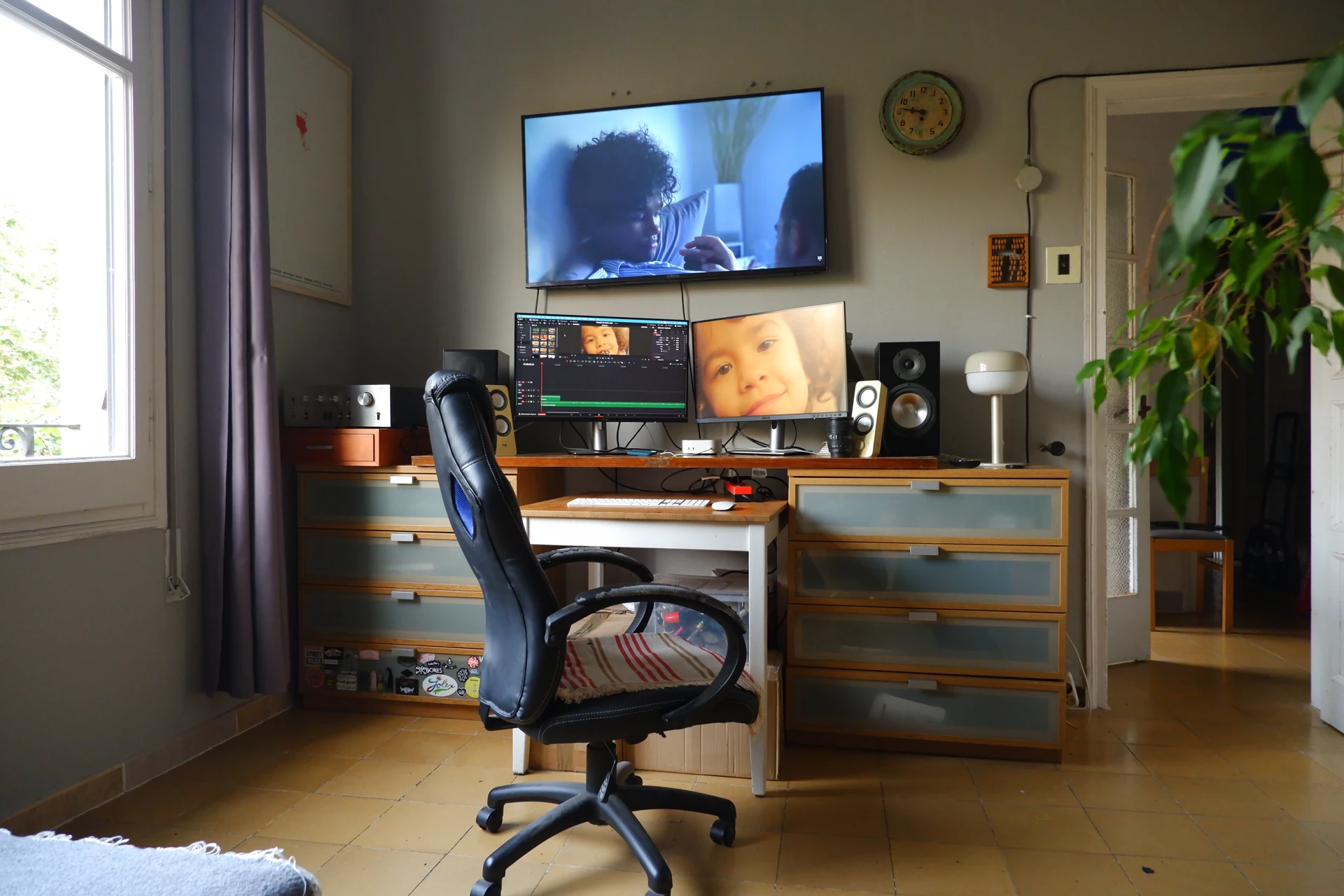 Sala de muntatge amb tres pantalles, taula de fusta i llum natural.